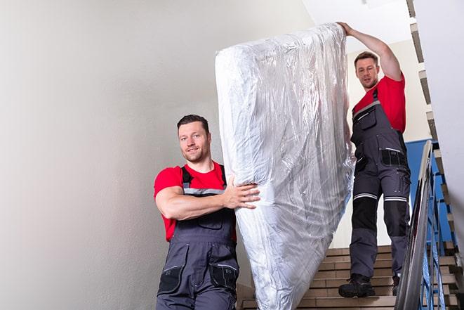 workers maneuvering a box spring through a narrow hallway in Five Points