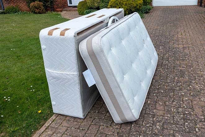 a mattress being hoisted by two workers into a dumpster